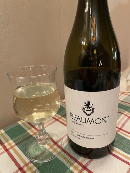 A glass of white wine sitting on a table next to the wine bottle with ‘Beaumont’ written on the label