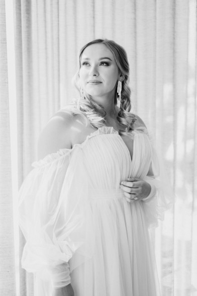 Bride in her dress backlit by white curtains 