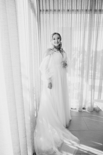 Bride in her dress backlit by white curtains 