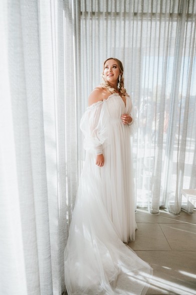 Bride in her dress backlit by white curtains 