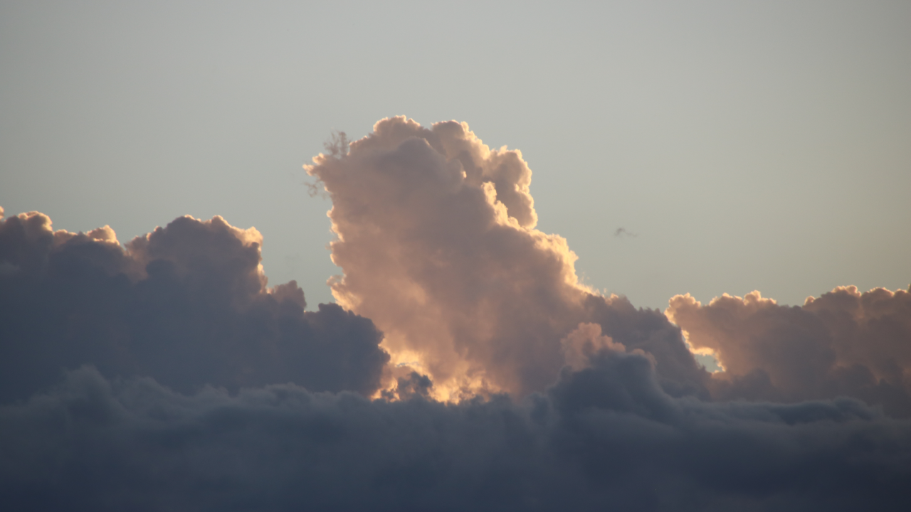 A photo of a lit cloud billowing above shadowed cloud banks at set