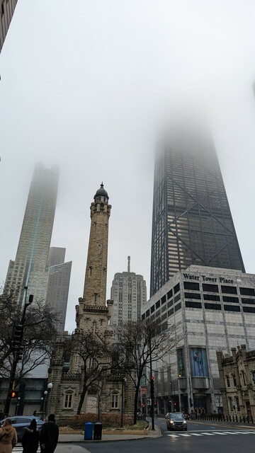 Looking north on Michigan Avenue in Chicago. The famous Gothic -style Water Tower is in the foreground. Across the street to the right is the Water Tower Place shopping complex. The 96-story John Hancock Building rises up behind Water Tower Place. It was a damp day, so the upper floors of the Hancock are obscured by low clouds.