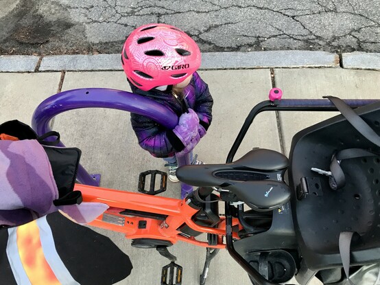 Toddler wearing a bike helmet clutching the purple bike rack, unwilling to let it go. 