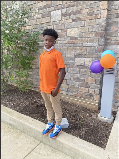 Photo of Karon Blake standing. Wearing khaki pants and an orange shirt. 