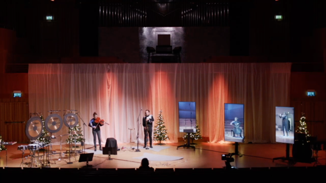 Musicians on stage at Studio Acusticum in Piteå playing with musicians at UdK Konzertsaal in Berlin  shown on stage on vertical monitors.