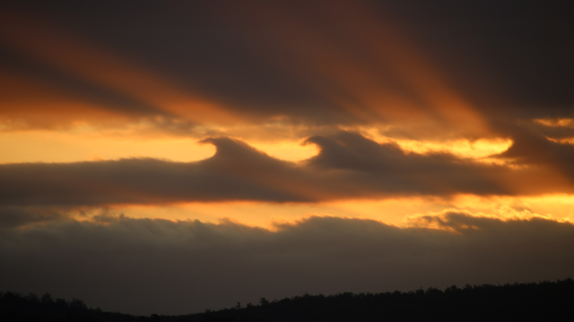 Light shafts from the setting sun, cast up and through wave-shaped clouds