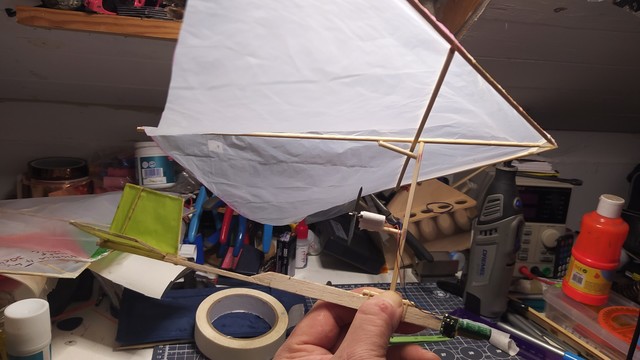 A tiny bamboo skewer and pedal bin liner Rogallo wing model with a stick fuselage holding a supercapacitor and motor setup. 