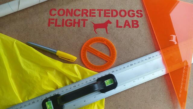 Pasting table workbench with a "ConcretedogsFlightLab" sticker on it. The bench is covered in drawing tools, some of them lasercut out of orange plastic. 