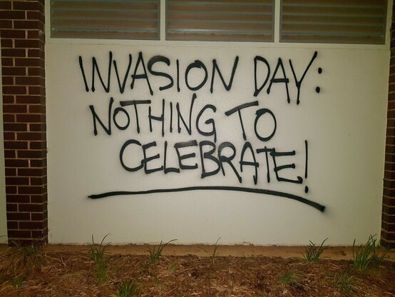 "Invasion Day, nothing to celebrate" painted on a wall with black spray paint 