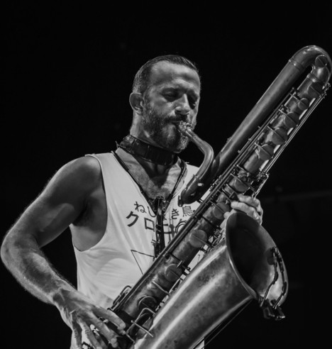 A black and white photo of the saxophonist Colin Webster by Daniele Maldarizzi, playing his bass saxophone.