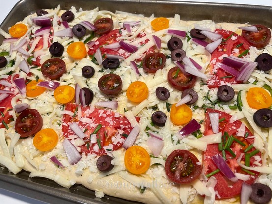 Before baking: the focaccia uncooked, the top decorated with previously mentioned toppings just before it goes into the oven.