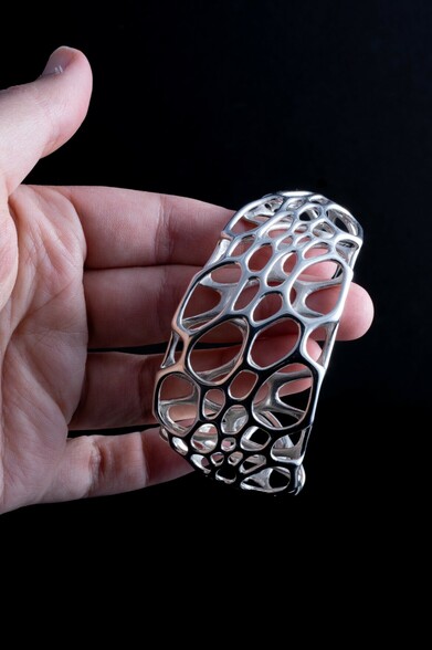 hand holding a sterling silver cuff bracelet composed of an intricate cellular web of bubble-like forms
