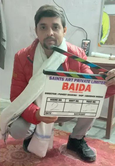 Actor Vishnu Mishra squats in a sparse room wearing a thick red down jacket, a white stole with a pale blue stripe, grey-white trousers and black trainers, holding a clapper board that shows the production company for the film as "Saints Art Private Limited" and the working title as "Baida". Puneet Sharma is noted as director on the clapper board, and Abhishek Modak is named as director of photography. The photograph was posted to Instagram by Mishra on Thursday.
