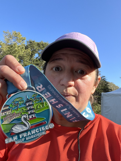 A pink-faced woman tiredly holding up a half marathon finisher medal