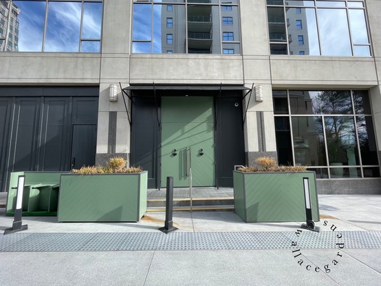 Two green planters and the matching front door at the entrance to the building. The planters are filled with dead plants, soon to be removed. A reflection of the blue sky can be seen in the windows above the front doors.