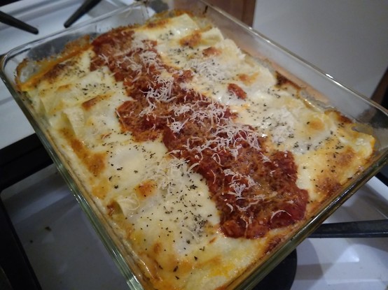 A dish of cannelloni is light colored with a strip of tomato sauce and some browned bits