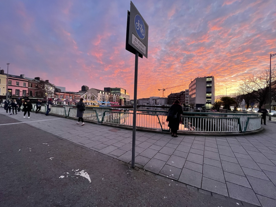 Reflections of a sunset over Cork buildings & river & people taking the photograph. 