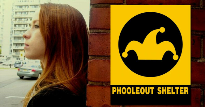 A woman with long red hair and a determined look in her eye, Anna in Kokomo Indiana, rests with her back against a brick wall, facing toward the left. On the brick wall, a sign for the PhooleOut Shelter hangs. The sign’s design, created by Anna, echoes Fallout Shelter signs produced by the US Civil Defense Administration in 1961.