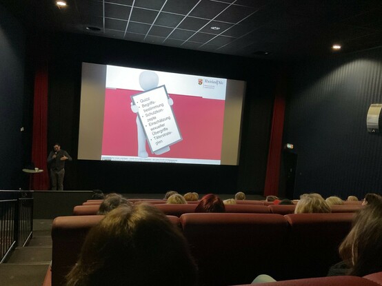 Workshop im Kino, ein Vortragender spricht, im Hintergrund eine Präsentation auf der Leinwand