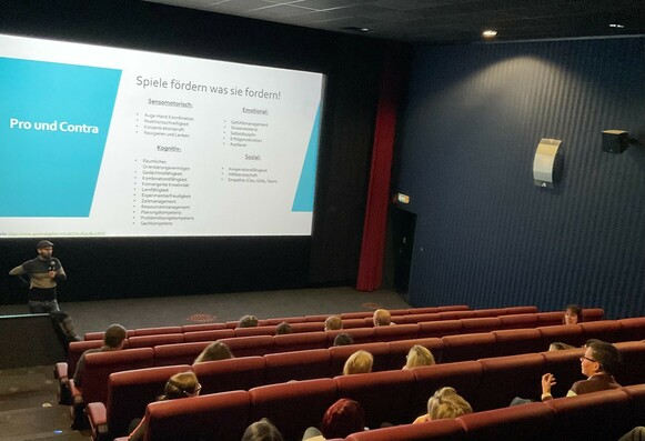 Workshop im Kino, ein Vortragender spricht, im Hintergrund eine Präsentation auf der Leinwand
