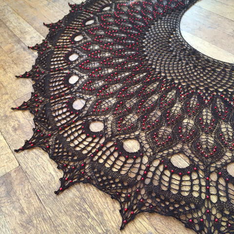 Closer view of the black shawl. The red beads are reflecting the light so they're very visible. Some of the holes in the lace are especially large, with lots of stitches growing out of them into a net-like pattern at the edge of the shawl.