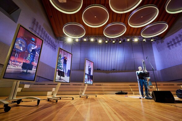 Four musicians playing on stage. Three are shown inside vertical screens.