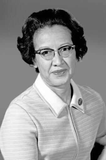 A black and white photo of Katherine Johnson. She is wearing a top with thin stripes, a zipper down the front, and a pin on the collar. Johnson is looking directly at the camera and has a slight smile.