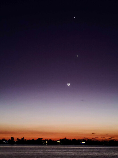 A photo of the night sky shortly after dusk, with the moon, venus, and jupiter all showing bright and clear one above the other.