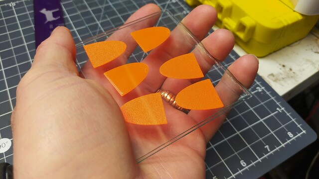 Hand holding two roughly 10cm square glass plates. Sandwiched between them are 6 small 3D printed eliptical fins. 