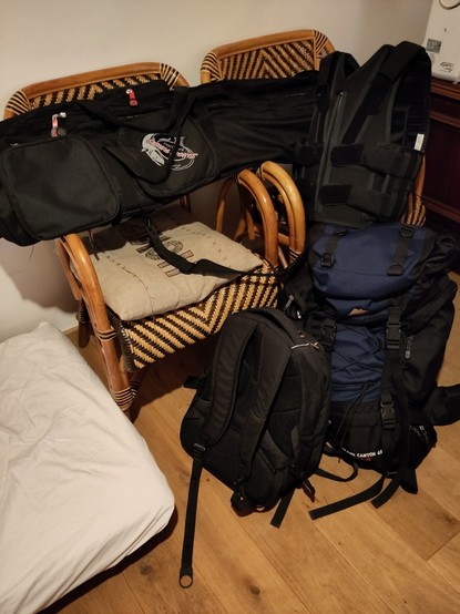 Two big packed backpack, a large bag for fishing rods and a tactical anti stab vest on a chair