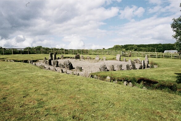 A view of the site taken from the right hand side of the previous image. This one shows the same circle and cairn, but also the stone row alignment.

The row is made up of small stones, no more than 30cm tall, and one end of it reaches the cairn’s kerb. The surface level of the site makes the stone row and circle look as though they are dug down into the soil.