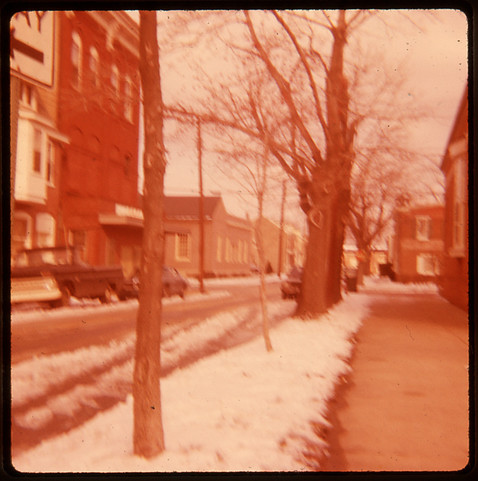 Slightly blurry, faded color transparency image looking down Fifth Street in New Castle, Delaware past the Library. The post office and old Earle Theater can be seen to the left.