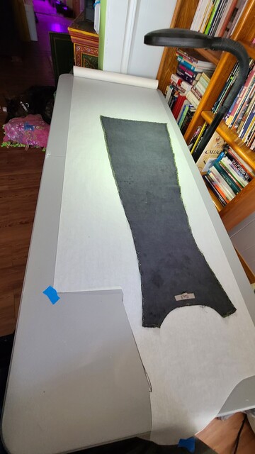 Black center back piece of the deconstructed dress laid flat on white pattern paper leaving extra room at the bottom for extending the hem. 