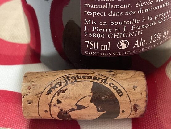 Wine cork on which a silhouette of someone drinking from a wine glass is shown. The red label (with white writing on it) is shown in the background 