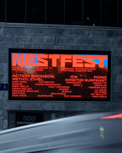 NestFest billboard with orange letters on brown and light blue background, on a wall in the street.