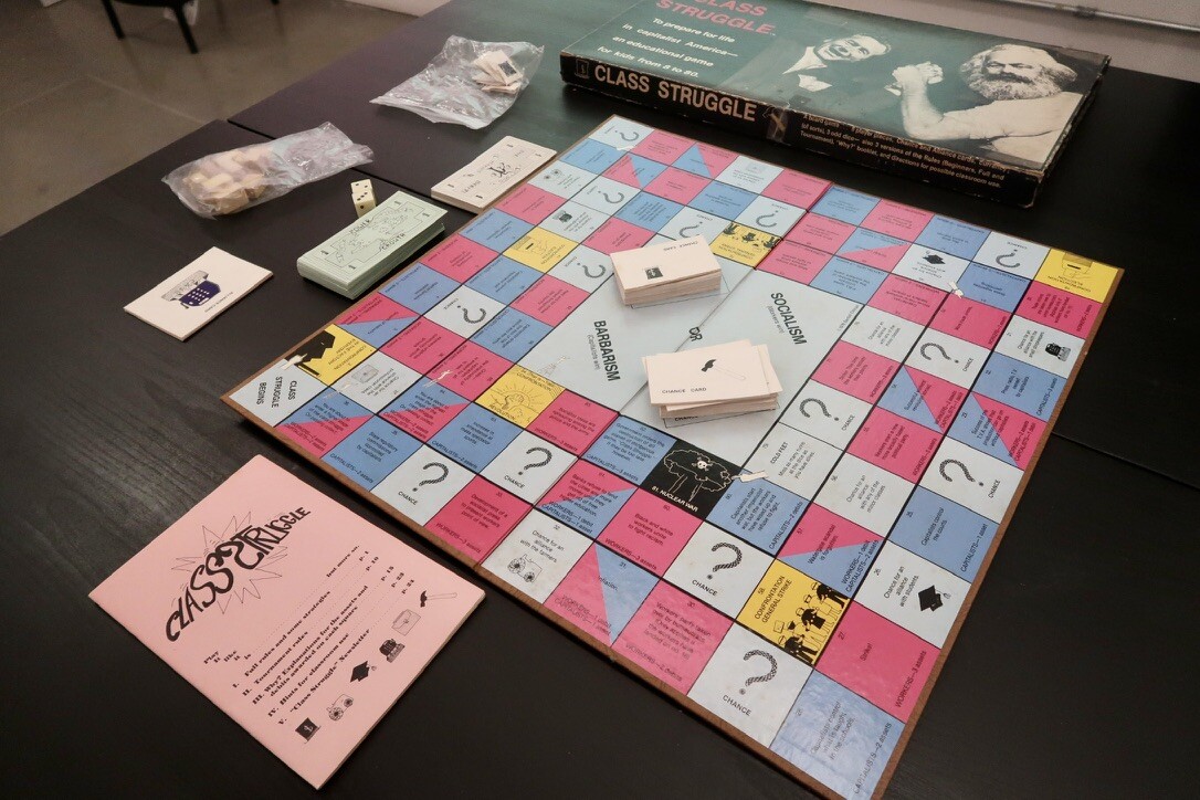 A photo of Class Struggle laid out on a table ready to be played. The board resembles Monopoly, but with 3 rows of tiles on the outer edge, instead of just one.