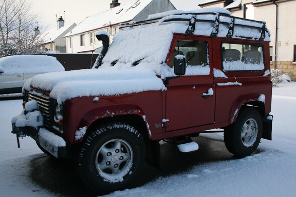 Red Landrover Defender covered by snow.