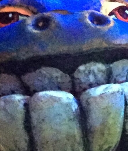 A picture of a odd blue hued monster with humongous teeth slightly grainy. Looks like an alien with a big head and is super high