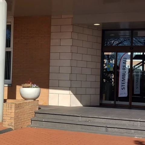 Ingang van het gemeentehuis in Wierden met in het raam een reflectie van de banner met daarop stembureau.