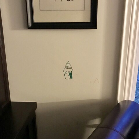 Unfinished drawing of a house in indelible marker pen directly on a living room wall, drawn by a small child, hence low down the wall. 
