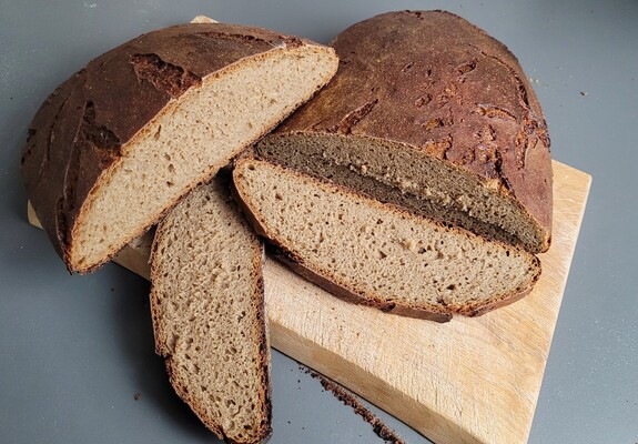 Auf einem Schneidebrett liegt ein ovaler Laib Brot, teilweise aufgeschnitten. Er ist relativ flach und die Krume ist mittelporig. 