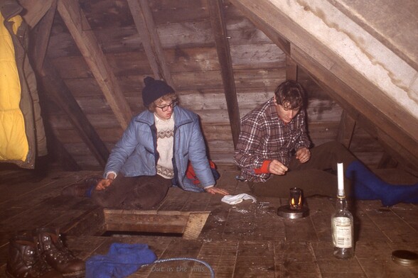 Young man playing with lighting candles and a burner in the upstairs area of a mountain bothy. Wooden floor and beams and roof make this a hazardous occupation. Another young man watches uncertainly.