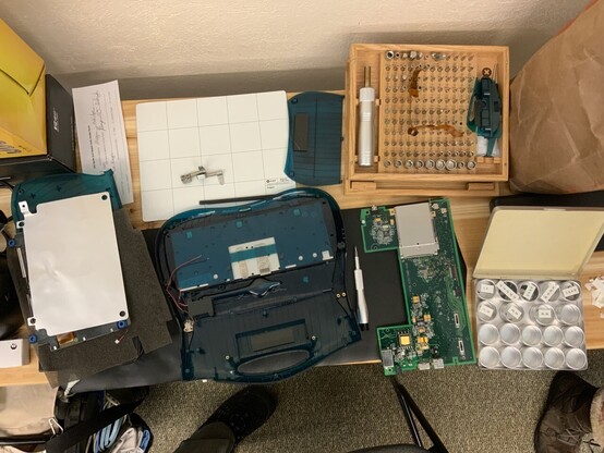 A disassembled Apple eMate 300 laid out on an anti-static mat on a table, with iFixit magnetic project mat and universal bit kit in view.