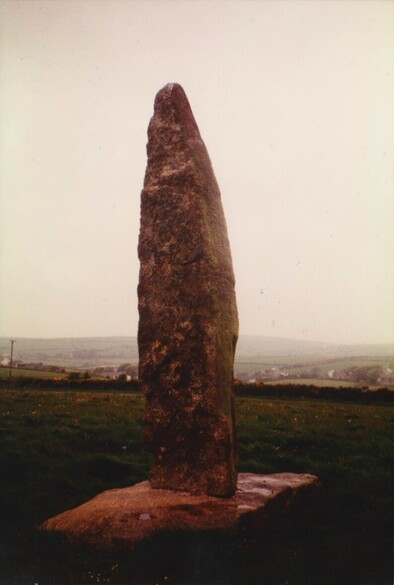 The prehistoric standing stone on Lezerea Farm in Cornwall. The large modern diamond-shape concrete base is visible at the bottom.