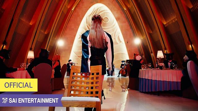 cover poster for the craxy music video 'nugudom'.
photo shows a person with long hair from behind, walking away from the camera while dragging a chair. in the room there are people sitting at several dinner tables and in the back there is a band playing classical instruments. all the people in this room are wearing animal (dog) heads/masks.