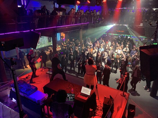 A photo of the crowd at DNA lounge. It’s a big crowd with people dancing on the main floor and watching from the second floor. Many are wearing masks. 
