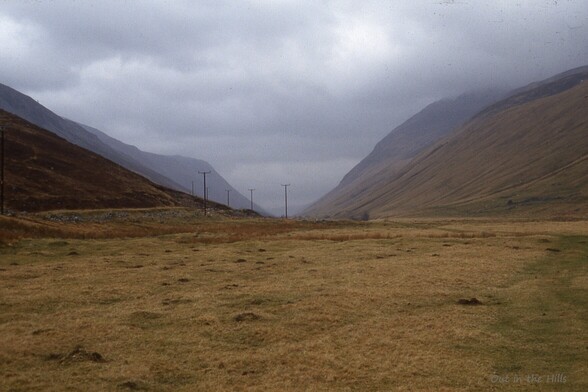 Looking along a long straight valley, flat with steep sides. A line of telegraph poles receding into the distance. Dull and cloudy.