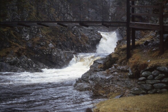 A full waterfall under a wooden foot bridge.