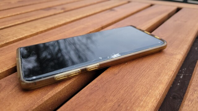 A Samsung Galaxy S10+ lying flat on a table, its screen is broken, below the screen protector.