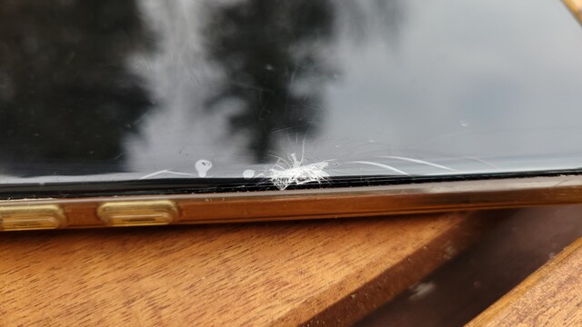 A Samsung Galaxy S10+ lying flat on a table, its screen is broken, below the screen protector, a close up shot.
